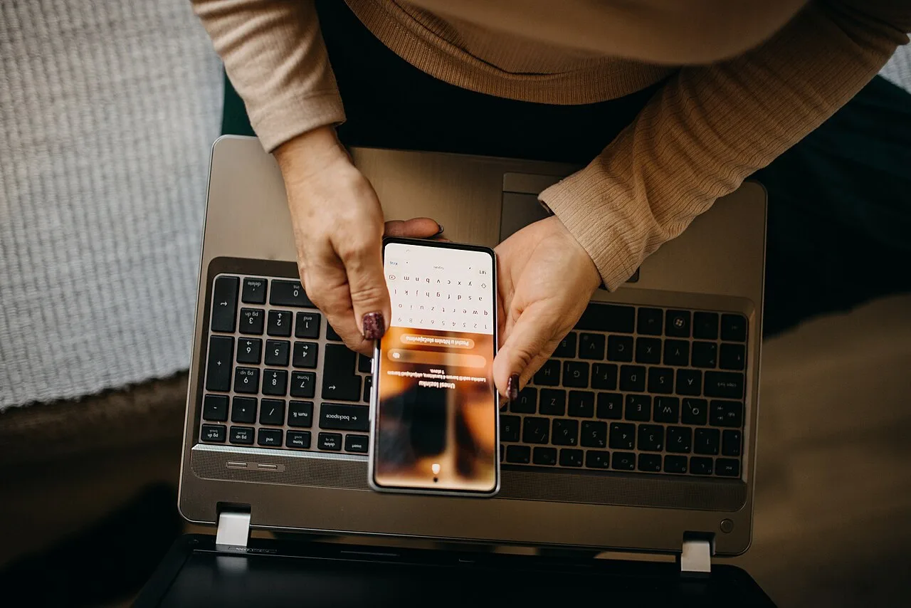 A middle aged woman using a smartphone beside a laptop